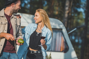 handsome smiling man cutting avocado while girlfriend with wine looking at him