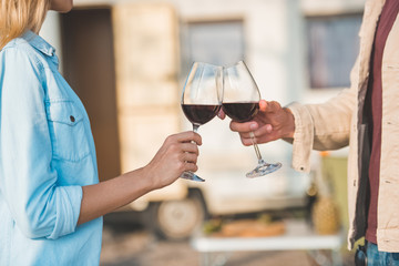 cropped view of couple clinking with glasses of red wine near campervan