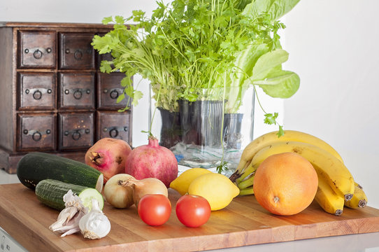 Vegetables, herbs and fruits on a clean table, granate apple, lemons, grape fruit, bananas, all white kitchen interior with coriander, parsley, salad, garlic, zuccini, cucumber, tomatoes, onions