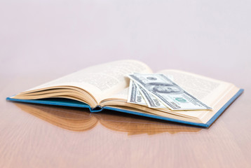 Open book on a glassy table with 100 us dollar banknotes on the page, closeup