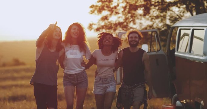 The multicultural friends have a great time together at the nature , holding each other and walking through the field , background amazing sky lights