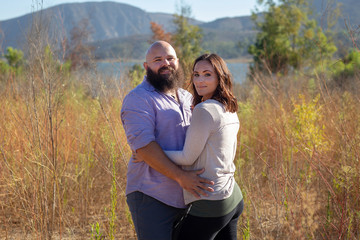 Happy couple standing in grass field holding each other overlooking mountains