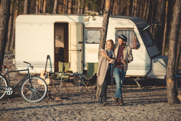 happy couple with glasses of wine walking near trailer in camp