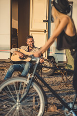 selective focus of girl with bicycle and man playing guitar near trailer