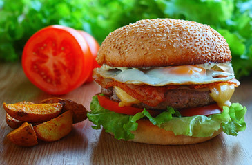 Juicy burger with beef patch, cheese, bacon, tomatoes, salad, quail eggs. On the table among fresh vegetables