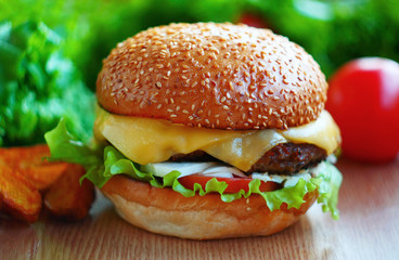 Juicy burger with beef patch, cheese, tomatoes, salad. On the table among fresh vegetables