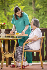 Nurse serving healthy breakfast to happy senior woman on terrace