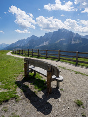 Hözerne Sitzbank mit Schatten vor Berggipfeln und blau weissem Himmel, 3 zinnen Bahn, Südtirol,...