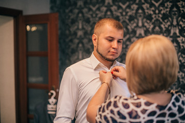 Mother is helping with a bow-tie to her son. Dressed and preparing her son for the wedding...