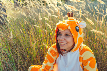 Girl smiles. Funny giraffe costume, Emotional student in funny pajamas sitting in a field of wheat....