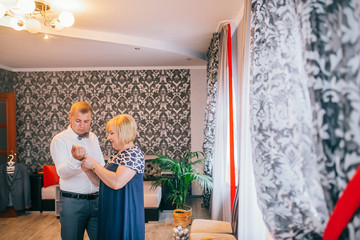 Mother is helping with a bow-tie to her son. Dressed and preparing her son for the wedding...