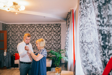 Mother is helping with a bow-tie to her son. Dressed and preparing her son for the wedding...