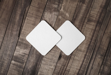 Two blank square beer coasters on wood background. Flat lay.