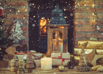 Christmas composition, lantern, presents and decorations on the table in front of fireplace with woodburner, Christmas tree with baubles and ornaments and garlands, snow, selective focus, toned