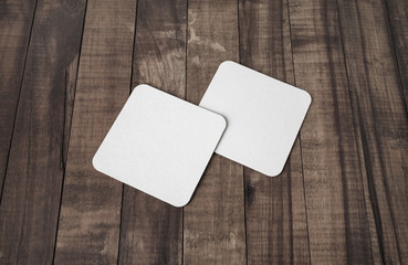 Blank white square beer coasters on wooden background.