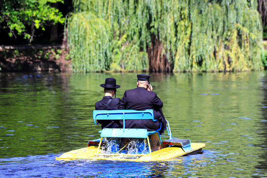 2 Hasidic Jews in traditional black clothes ride a catamaran on the lake in the autumn Park in Uman, Ukraine, during the Jewish New Year,  Orthodox Religious Jew