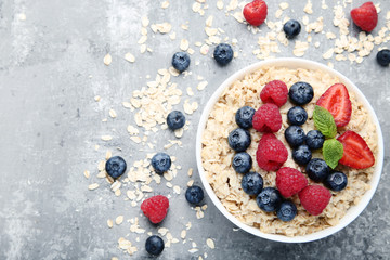 Oatmeal with berries in bowl on grey wooden table