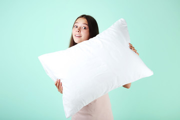 Young girl with white pillow on mint background