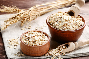 Oatmeal in bowls and scoop on wooden table