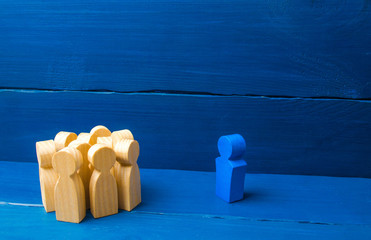 The crowd of wooden figures of people stand distantly and look at the blue man. The person tries to...