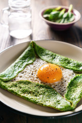 Gluten free spinach crepe with fresh egg on a wooden background