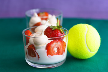 Wimbledon inspired whipped cream, meringues and fresh strawberries in a glass bowl on a green and...