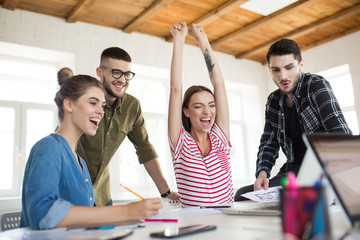 Fototapeta na wymiar Group of cheerful business men and women happily working together in office. Young emotional people joyfully spending time at work