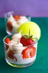 Wimbledon inspired whipped cream, meringues and fresh strawberries in a glass bowl on a green and violet background with a tennis ball