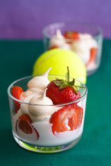 Wimbledon inspired whipped cream, meringues and fresh strawberries in a glass bowl on a green and violet background with a tennis ball