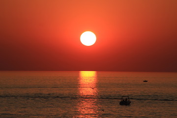 Red Sunset reflecting off water with boat sailing towards it 