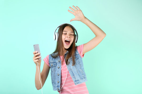 Young girl with headphones and smartphone on mint background