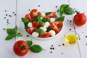 Caprese salad served on a white ceramic plate. White wooden background, high resolution