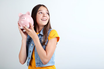 Young girl with piggy bank on grey background