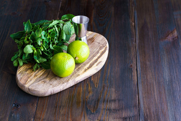 Fresh mint, limes and jigger on a wooden board. Dark background, high resolution