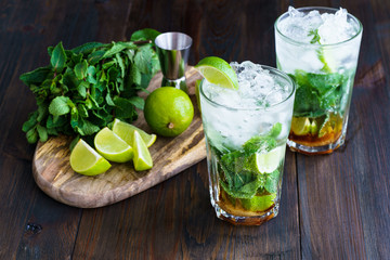 Dirty mojito and ingredients (fresh mint, sliced lime) served on a dark wooden board. High resolution.