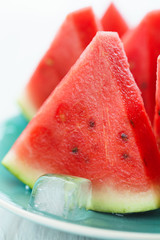Watermelon slices on a blue plate with ice cubes. White wooden background, high resolution