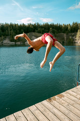 Young fit man jumping into a lake from a wooden jetty. Water sport. Nature and outdoor activity.