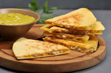 Traditional Mexican tortillas with a filling on a round wooden plate. Next to the bowl with a sharp green sauce guacamole. Close-up. Macro photography. 