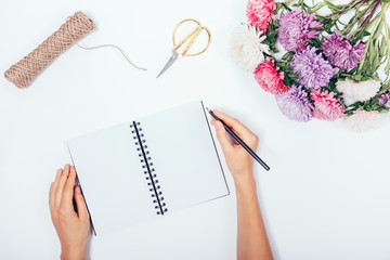 Female's hands writing in blank notepad among flat lay holiday border