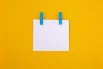 White paper with green clothespins on a bright yellow background.