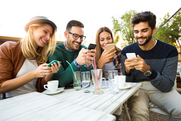Group of four friends having fun a coffee together. Two women and two men at cafe talking laughing and enjoying their time. Using phone