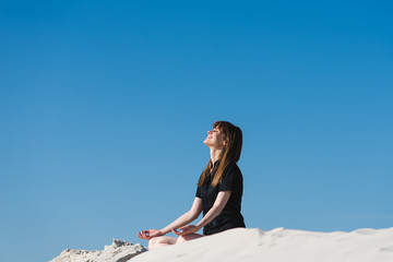 Smiling girl in lotus pose at sand dunes