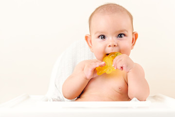 Cute baby infant kid biting sitting in highchair and chewing yellow eething toy copy space bright...