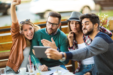 Group of four friends having a coffee together. Two women and two men at cafe talking laughing and enjoying their time using digital tablet.