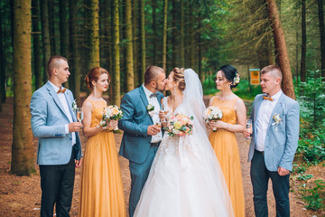Groomsman opens a bottle of champagne before newlyweds standing in the park. Wedding party in the...