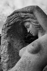 Female stone sculpture with a naked breast with a raised up hand touches the hair against the sky