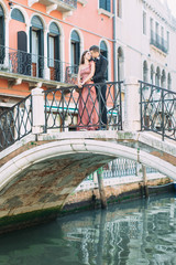 Fototapeta na wymiar Elegant couple stands on the bridge and enjoys the view to a canal in Venice, Italy