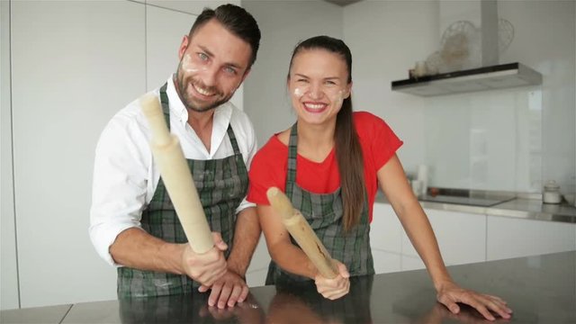 Couple Making a Funny Faces Together. Bearded Man and Girl with Caucasian Appearance in Aprons In Modern Kitchen.