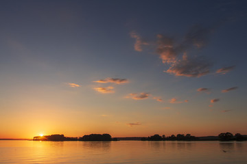 Obraz premium Landscape of sunset over the horizon on a beautiful lake. Colorful sky with clouds over the surface of the lake in the evening. Vivid sun sets over the horizon. Summer Landscape.