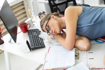 Young girl lies with closed eyes on documents on desk in office.
